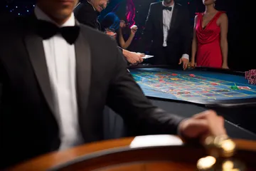 Um dealer profissional de smoking cumprimentando jogadores na mesa de roleta, simbolizando a autêntica sensação de cassino ao vivo no 44FF.